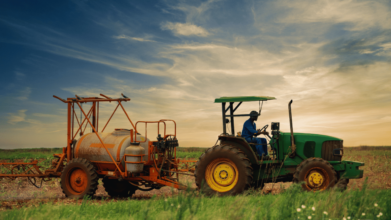 Farmer driving a green tractor with equipment across a field at sunset, symbolizing the hard work and dedication of family farms in Newfoundland and Labrador.
