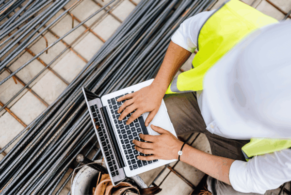 Construction worker in a safety vest using a laptop on-site, symbolizing the growing digital connectivity and cyber risks in the construction industry.