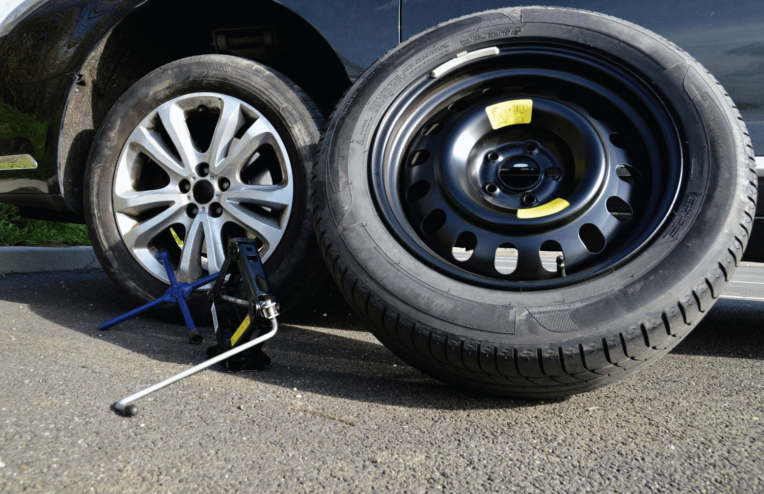 A car with a tire jack and spare tire being changed on the side of the road, illustrating practical Newfoundland and Labrador driving advice about maintenance and road safety.