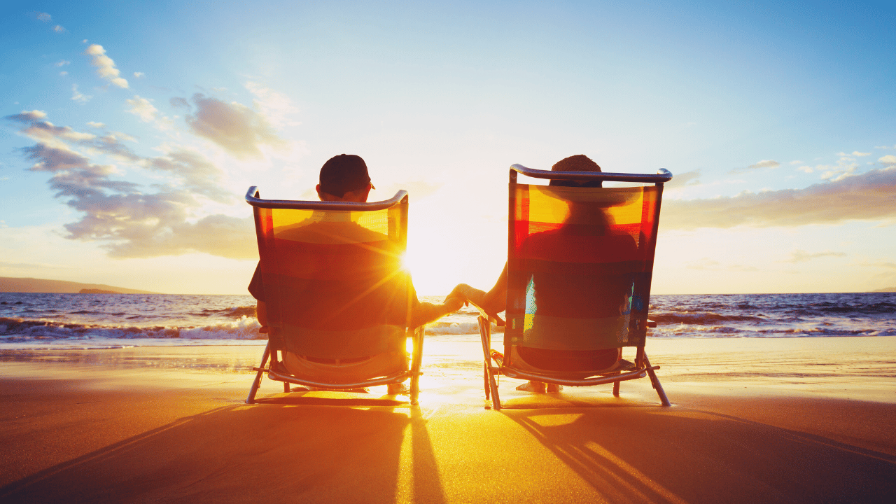 Couple sitting in beach chairs at sunset, representing travellers considering whether they need travel insurance before a trip.