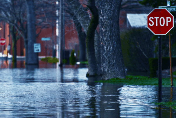 Flooded residential street with standing water surrounding trees and a stop sign, illustrating the risks of severe spring weather and flooding to neighbourhood homes.