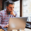 Business owner working on a laptop by a window in a modern office or café setting, appearing focused while reviewing information online. Image used for a blog about general liability insurance for businesses in Newfoundland.