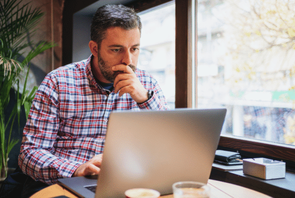 Business owner working on a laptop by a window in a modern office or café setting, appearing focused while reviewing information online. Image used for a blog about general liability insurance for businesses in Newfoundland.